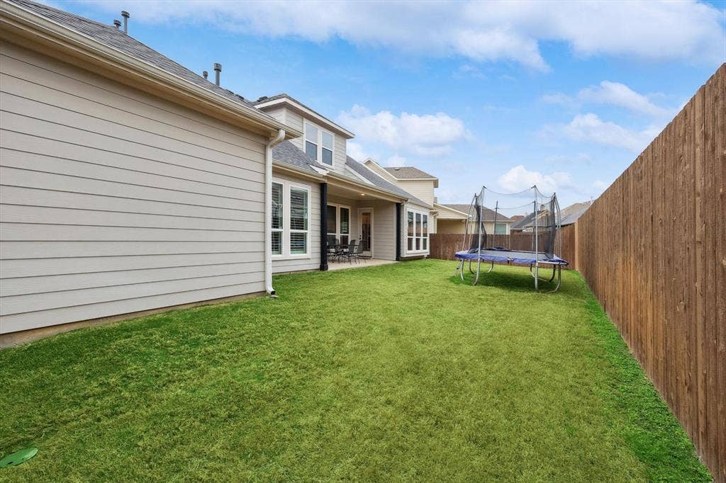 Expansive backyard featuring a manicured lawn, full privacy fencing, and a covered patio area