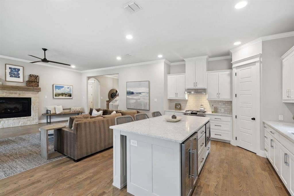 Open-concept living space with wood-finish flooring, a stone-surround fireplace, and a kitchen island featuring integrated beverage refrigeration
