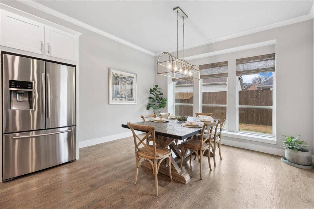 Stainless steel refrigerator, white shaker-style cabinetry, wood-finish flooring, contemporary linear chandelier, and triple windows with blinds