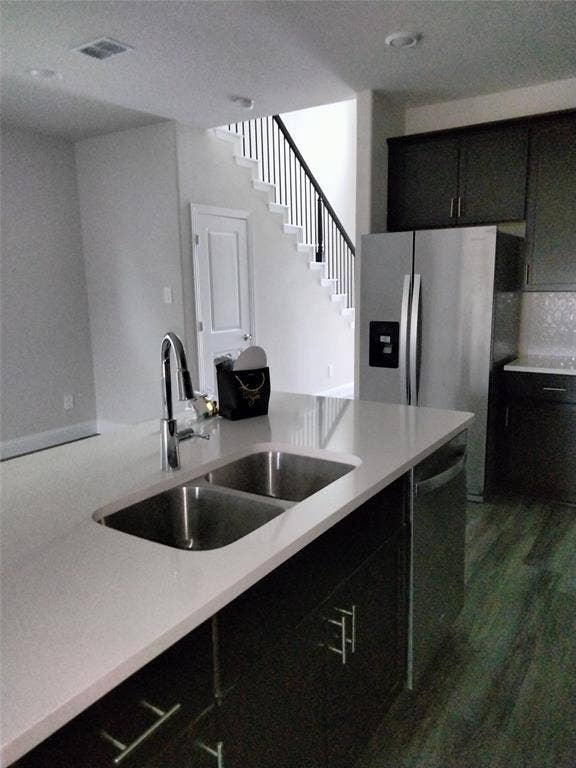 601 Willet Drive, McKinney, TX 75069 Kitchen island with an undermount double basin stainless steel sink, a pull-down faucet, light-toned countertop, and dark cabinetry