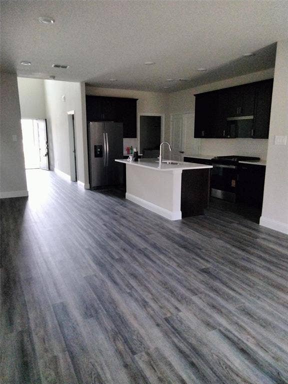 601 Willet Drive, McKinney, TX 75069 Open-concept kitchen featuring dark wood cabinetry, stainless steel appliances, a center island with sink, and light-toned countertops