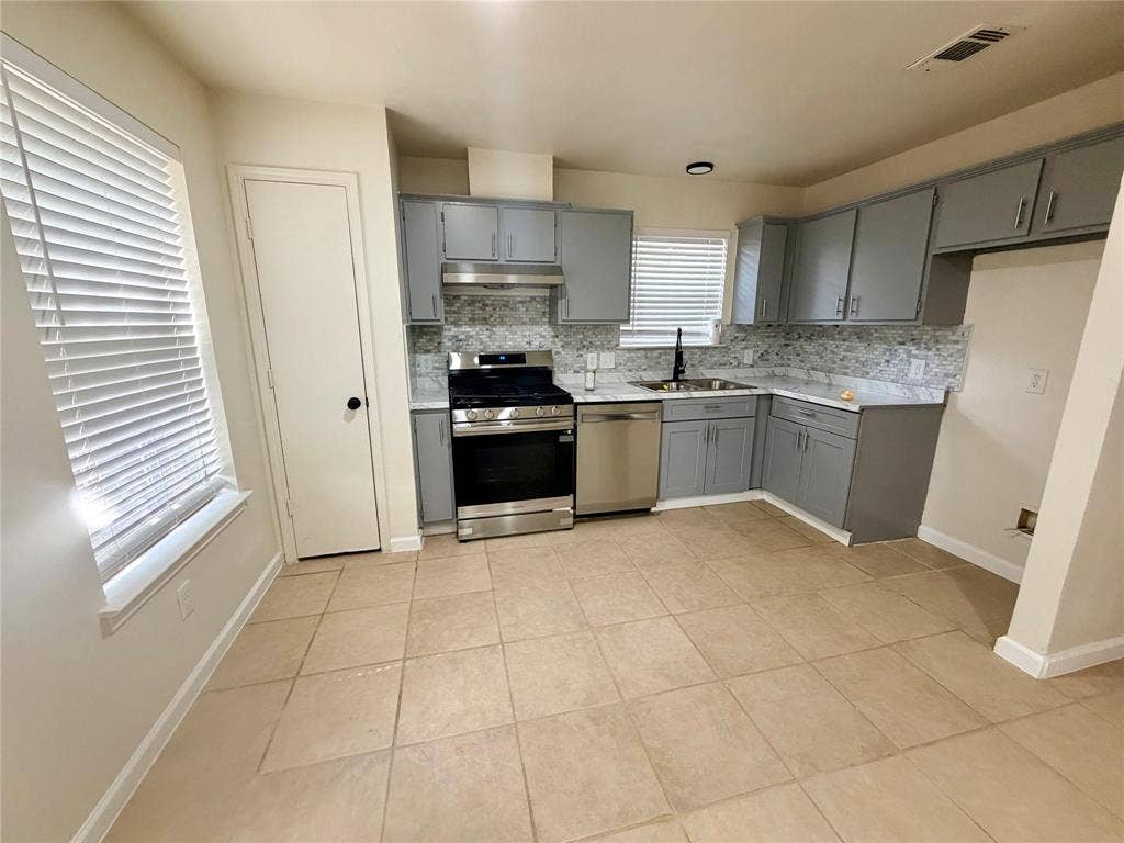 Kitchen featuring grey cabinetry, stainless steel appliances, mosaic tile backsplash, light-toned tile flooring, and white countertops