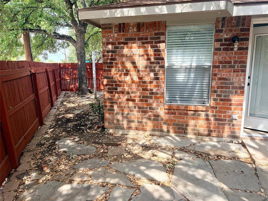 Brick exterior featuring a window with blinds, an exterior door with glass paneling, a stone patio, and a red wood fence