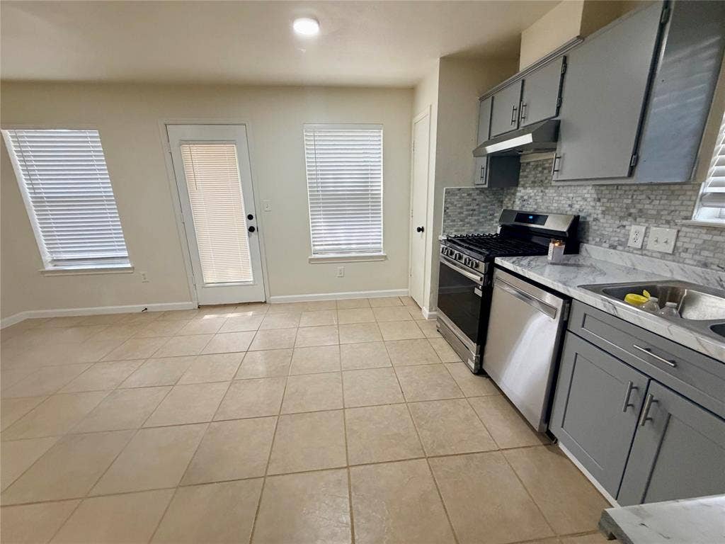 Kitchen with stainless steel appliances, mosaic tile backsplash, gray cabinetry, and light-toned tile flooring