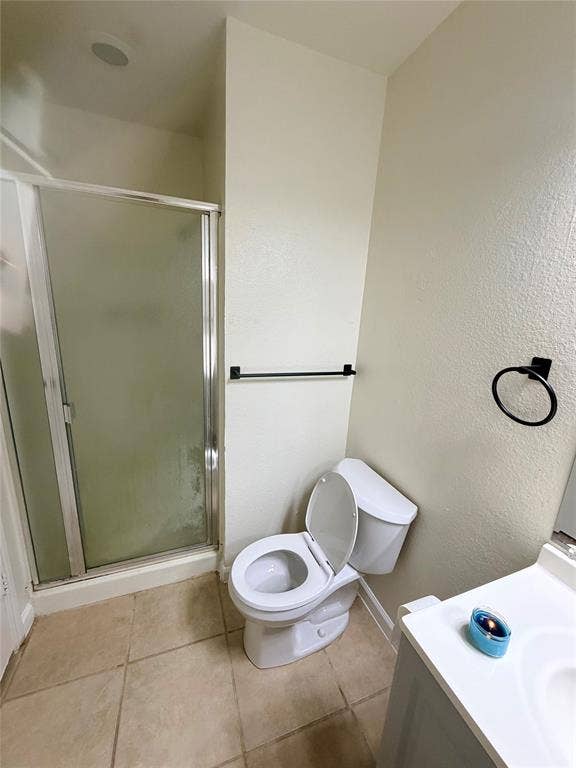 Shower enclosure with frosted glass, tiled flooring, white vanity with integrated sink, and modern black hardware