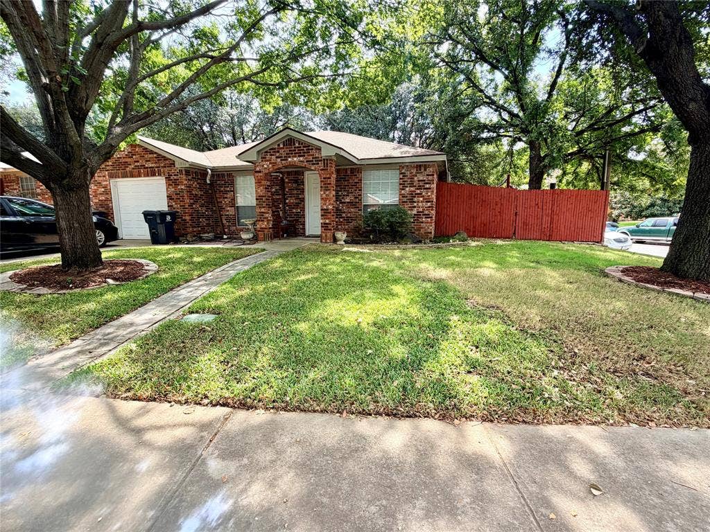 Red brick exterior with white trim, attached garage, concrete walkway, and a red stained wood privacy fence