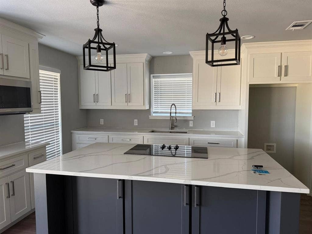 2928 Almeta Lane, McKinney, TX 75069 Kitchen featuring white upper and lower cabinetry, a dark-toned island with a light-toned countertop, and two pendant light fixtures
