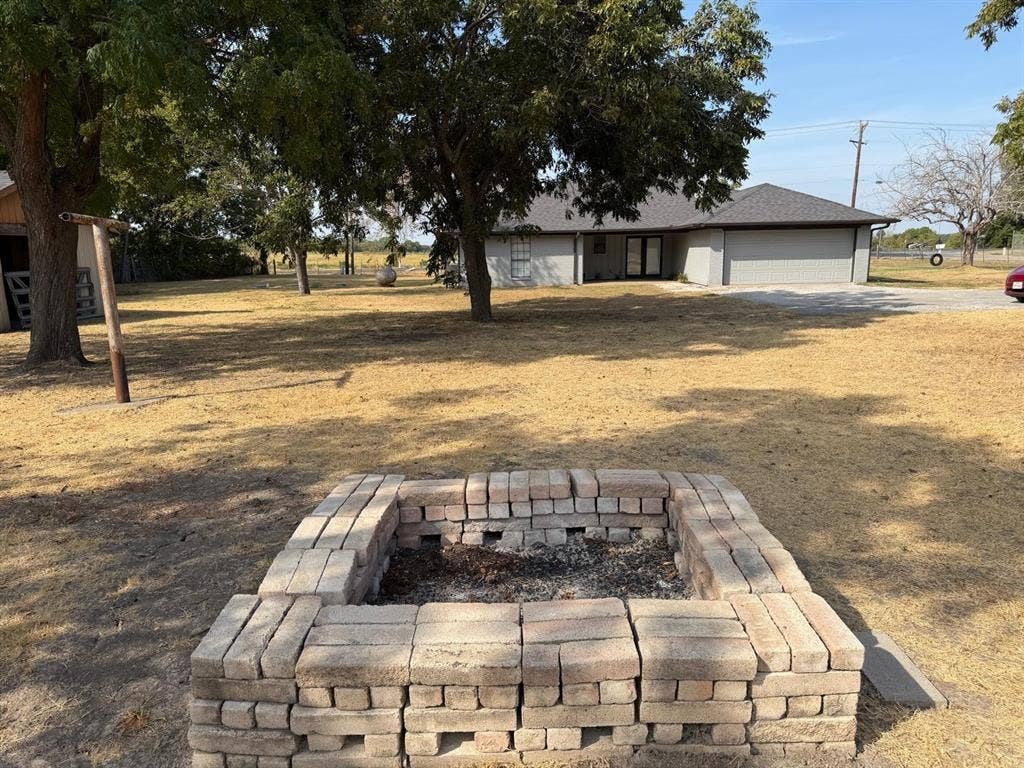 2928 Almeta Lane, McKinney, TX 75069 Backyard featuring a stone-block fire pit, mature trees, and a detached two-car garage