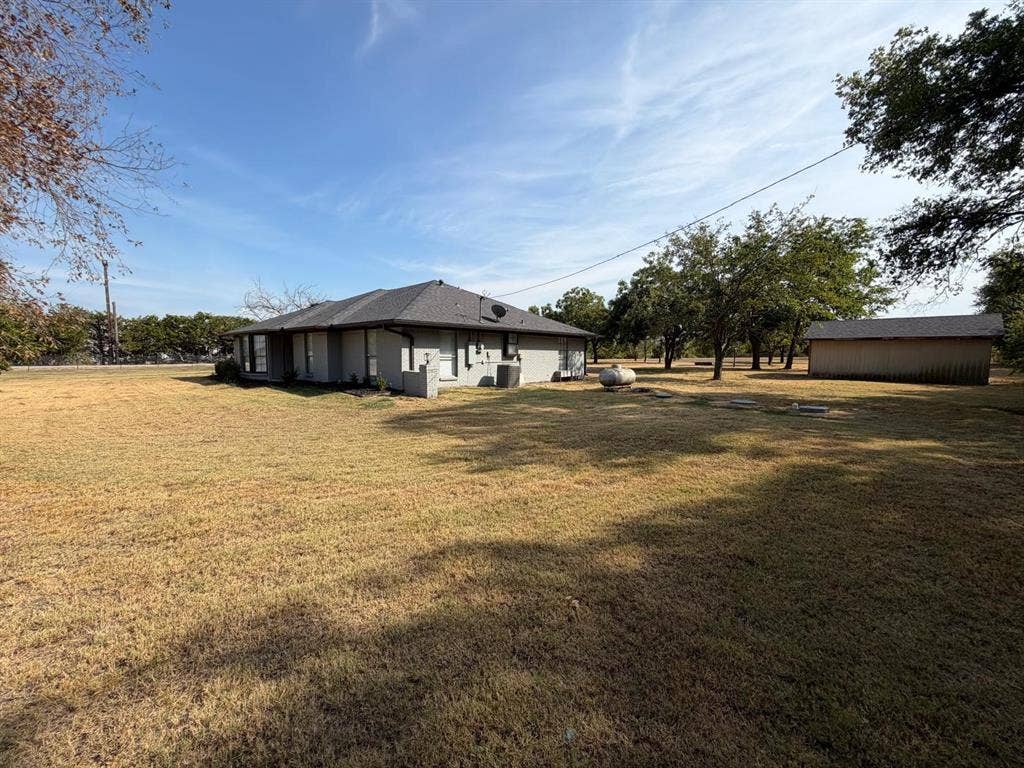 2928 Almeta Lane, McKinney, TX 75069 Single-story residence with a gray shingle roof, light-colored exterior siding, multiple windows, and a detached outbuilding