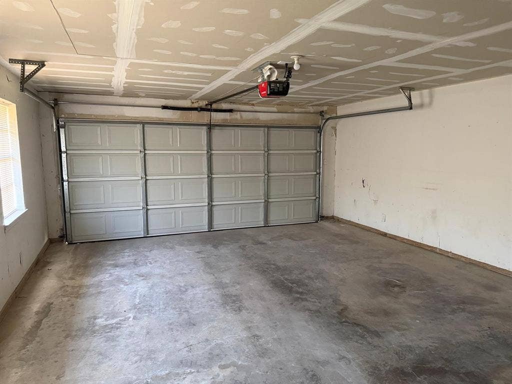 2928 Almeta Lane, McKinney, TX 75069 Concrete floor, white paneled garage door, exposed ceiling joists, window with blinds, garage door opener mechanism