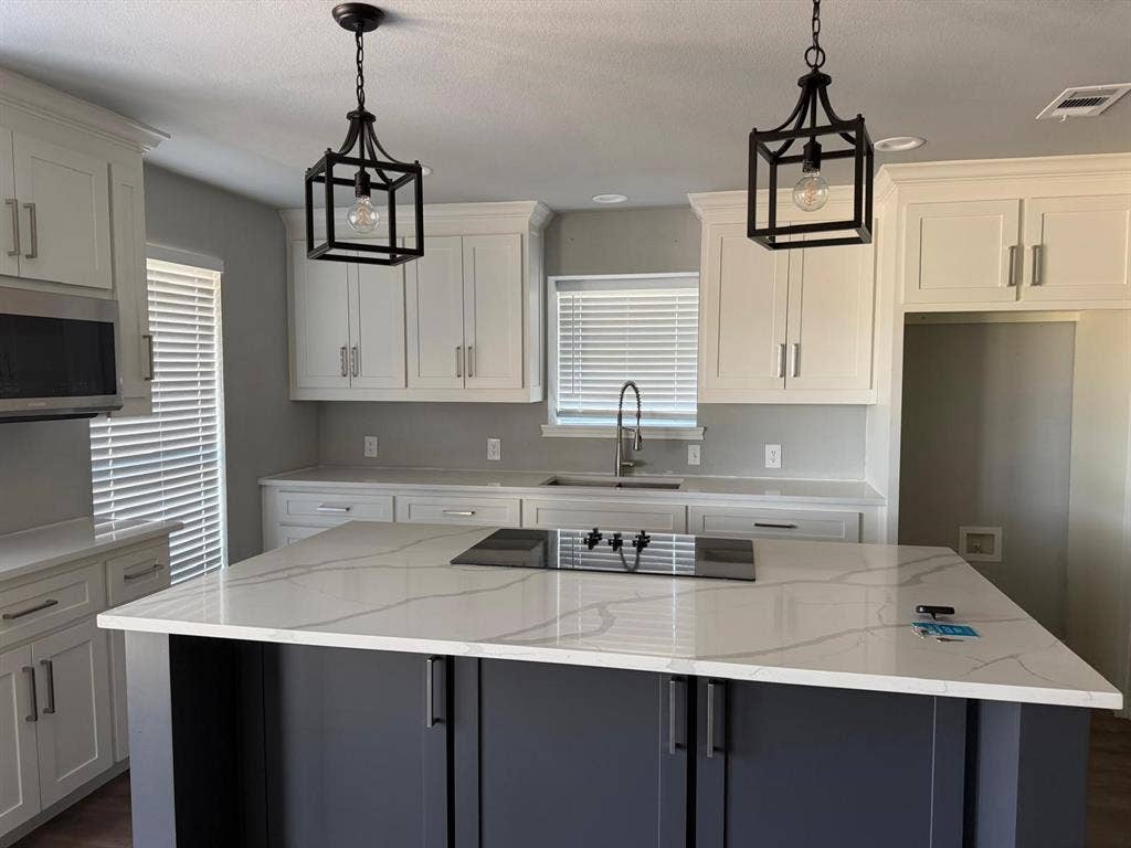 2928 Almeta Lane, McKinney, TX 75069 Kitchen featuring white shaker cabinetry, an island with a built-in cooktop, light-colored countertops with veining, a stainless steel microwave, and pendant lighting