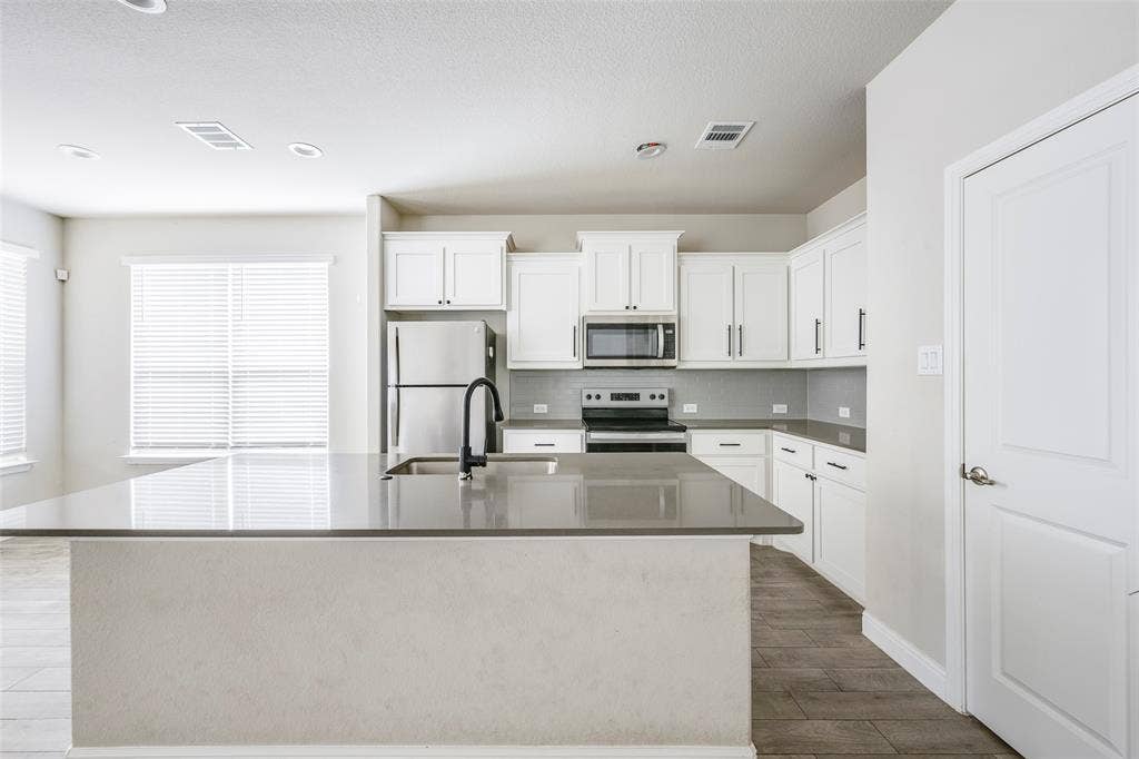 1548 Seabiscuit Drive, Granbury, TX 76049 Kitchen featuring a large island with a sink, stainless steel appliances, white cabinetry, and wood-finish flooring
