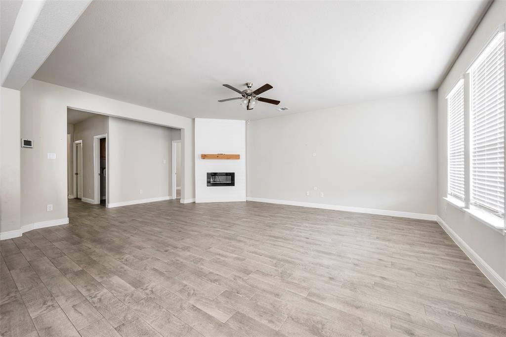 1548 Seabiscuit Drive, Granbury, TX 76049 Spacious room featuring wood-finish flooring, a contemporary fireplace with a wood mantle, a ceiling fan, and large windows with blinds