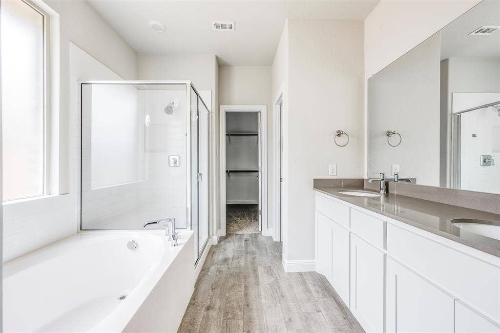 1548 Seabiscuit Drive, Granbury, TX 76049 Spacious bathroom featuring a built-in soaking tub, a clear glass shower enclosure with tile surround, a dual vanity with undermount sinks, and wood-finish flooring