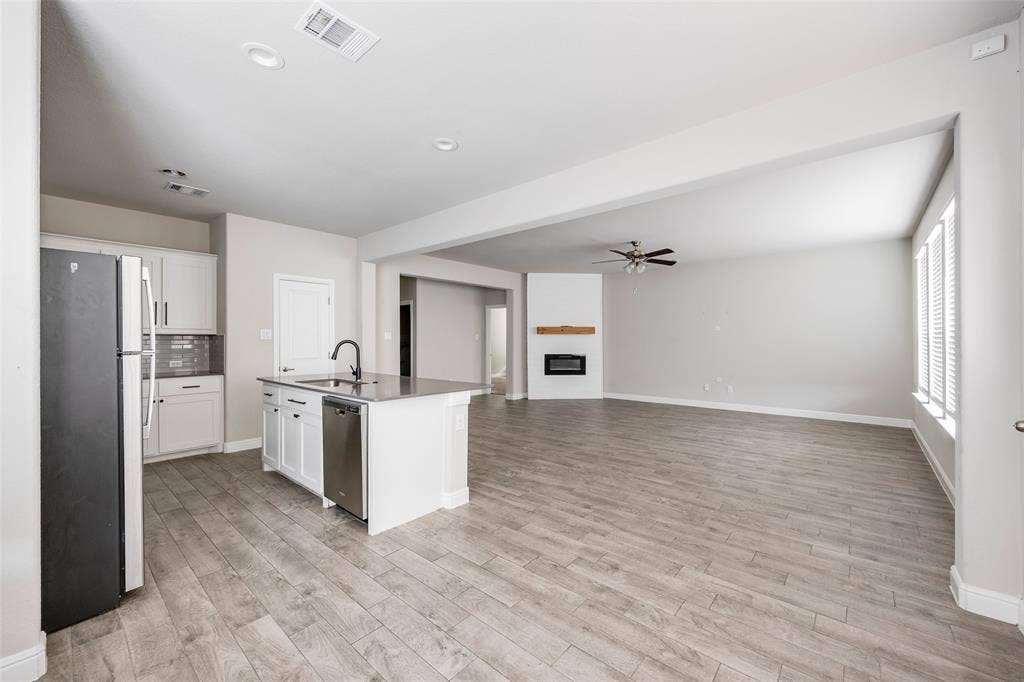 1548 Seabiscuit Drive, Granbury, TX 76049 Open-concept living space featuring wood-finish flooring, a kitchen island with sink and integrated dishwasher, recessed lighting, and a fireplace with a wood mantle