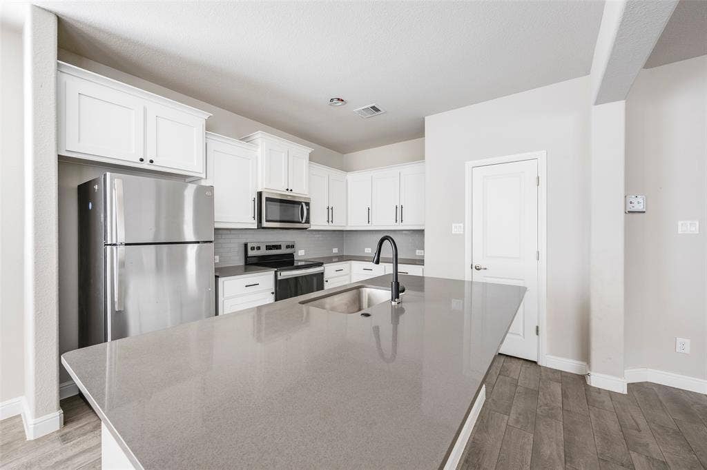 1548 Seabiscuit Drive, Granbury, TX 76049 Kitchen featuring white cabinetry, stainless steel appliances, a grey tile backsplash, grey countertops, and wood-finish flooring