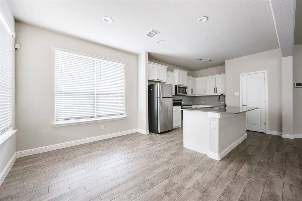 1548 Seabiscuit Drive, Granbury, TX 76049 Open-concept living space featuring wood-finish flooring, recessed lighting, and a kitchen with white cabinetry, stainless steel appliances, and a central island with a dark countertop