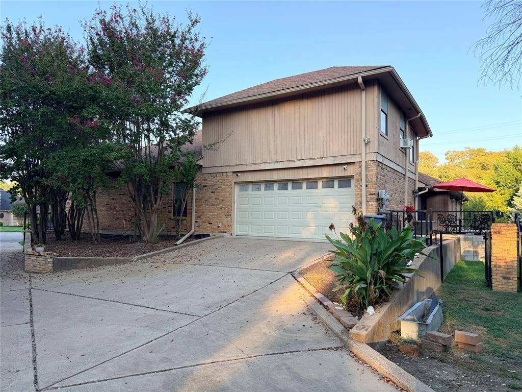 6801 Bellaire Court S, Benbrook, TX 76132 Rear entry garage, concrete driveway, and established plantings with view of back patio