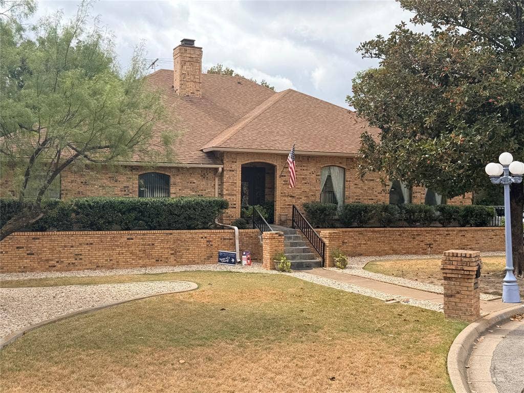 6801 Bellaire Court S, Benbrook, TX 76132 Brick exterior, integrated chimney, front entry staircase with wrought iron railing, manicured shrubbery, and a multi-globe lamp post