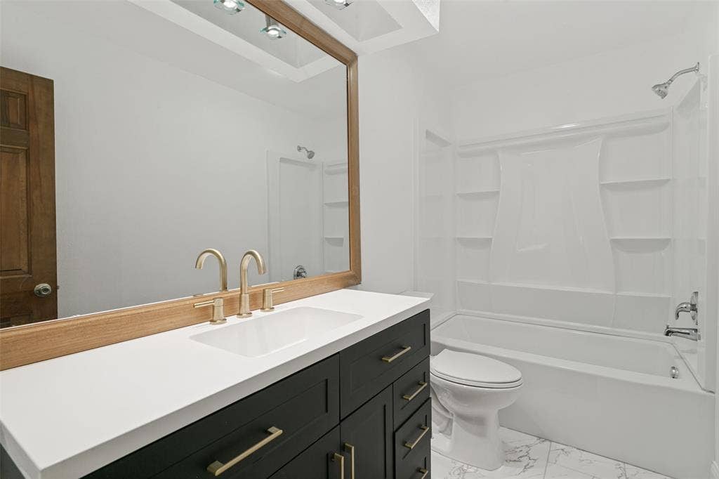 6801 Bellaire Court S, Benbrook, TX 76132 Vanity with a white countertop and gold-finish fixtures, large framed mirror, and a full bathtub with shower in upstairs bathroom