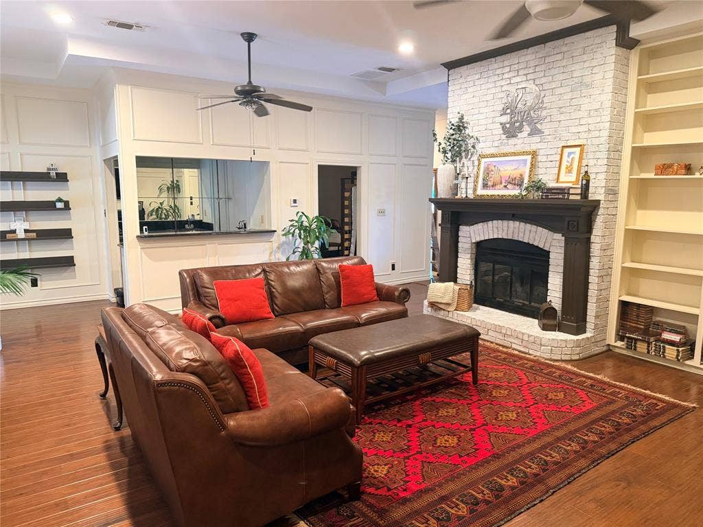 6801 Bellaire Court S, Benbrook, TX 76132 Wood-finish flooring, white brick fireplace with dark wood mantel, paneled walls, and a recessed ceiling with a ceiling fan