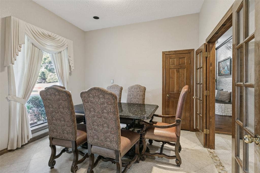 6801 Bellaire Court S, Benbrook, TX 76132 Recessed lighting with a textured ceiling, a large window with custom drapery, and wood interior doors with brass hardware enhance the dining room