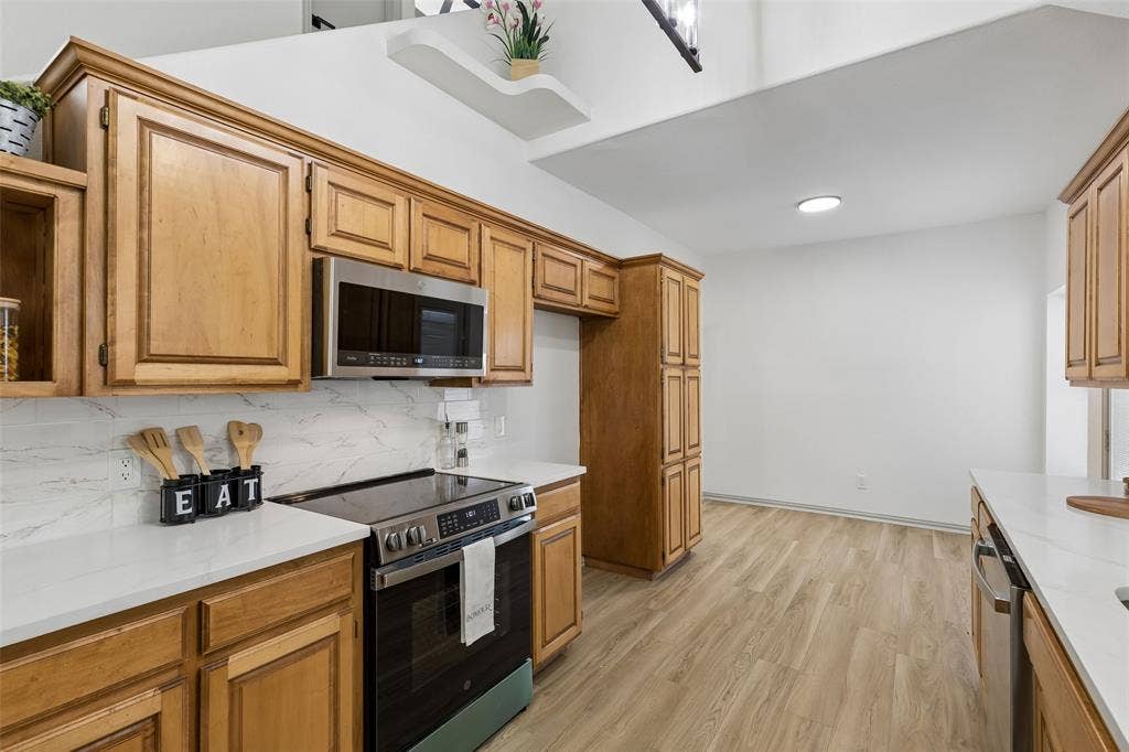 1503 Milla Court, Euless, TX 76039 Wood-finish flooring, wood cabinetry, stainless steel appliances, white countertops, and a white tile backsplash