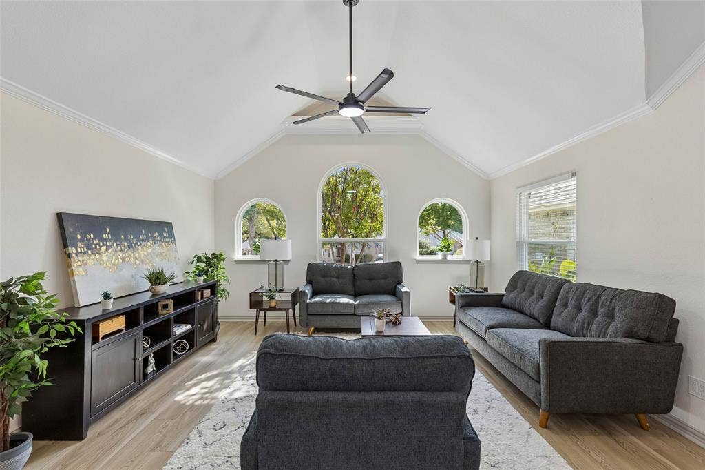 1503 Milla Court, Euless, TX 76039 Vaulted ceiling with a contemporary ceiling fan, three arched windows, crown molding, wood-finish flooring, and a built-in media console