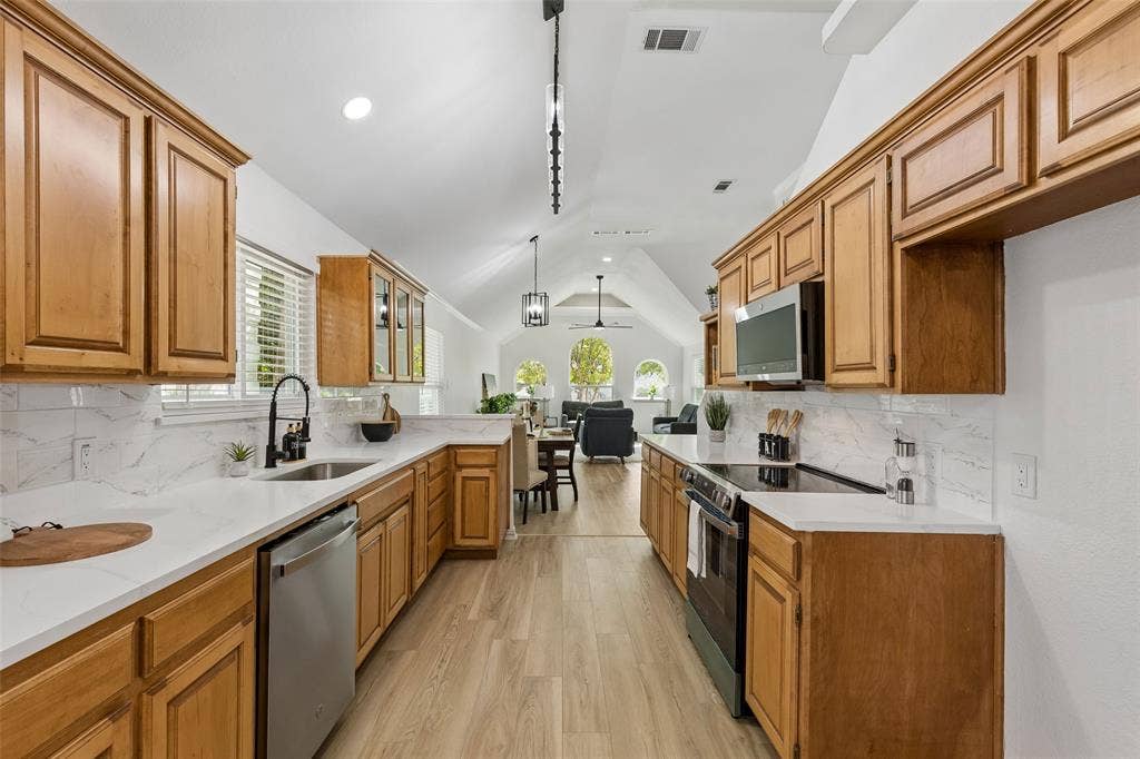 1503 Milla Court, Euless, TX 76039 Kitchen featuring light wood cabinetry, white countertops, stainless steel appliances, a white tile backsplash, and light wood-finish flooring