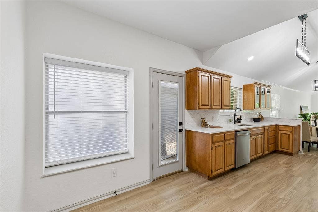 1503 Milla Court, Euless, TX 76039 Kitchen featuring wood cabinetry, light-toned countertops, a stainless steel dishwasher, and a black sink fixture