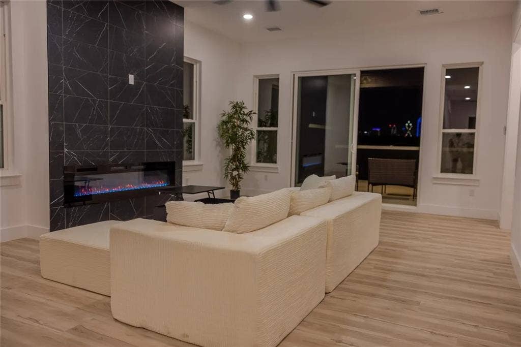 2806 Guymon Street, Dallas, TX 75212 Expansive living area featuring a full-height tiled fireplace with linear electric insert, wood-finish flooring, recessed lighting, and a sliding glass door to an outdoor space