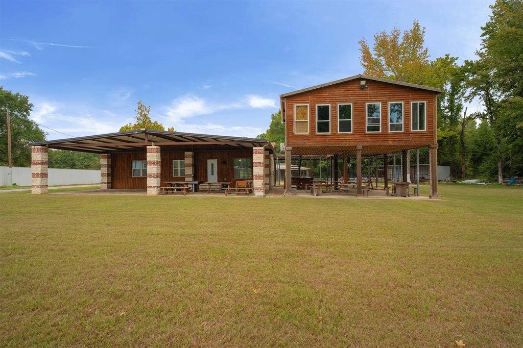5989 State Highway 31 E, Murchison, TX 75778 Two-story wood-sided structure featuring an elevated second level, a covered patio with brick and stone pillars, and a metal roof