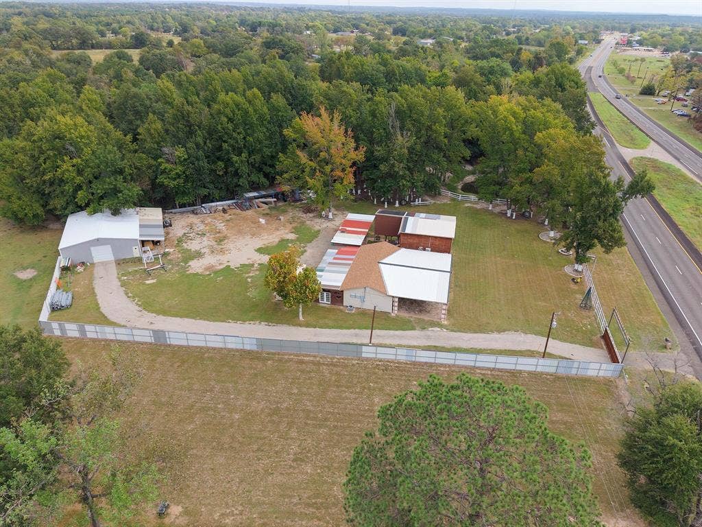 5989 State Highway 31 E, Murchison, TX 75778 Gated property featuring a main structure with a light-colored roof, a separate metal-sided outbuilding, a gravel driveway, and mature perimeter trees