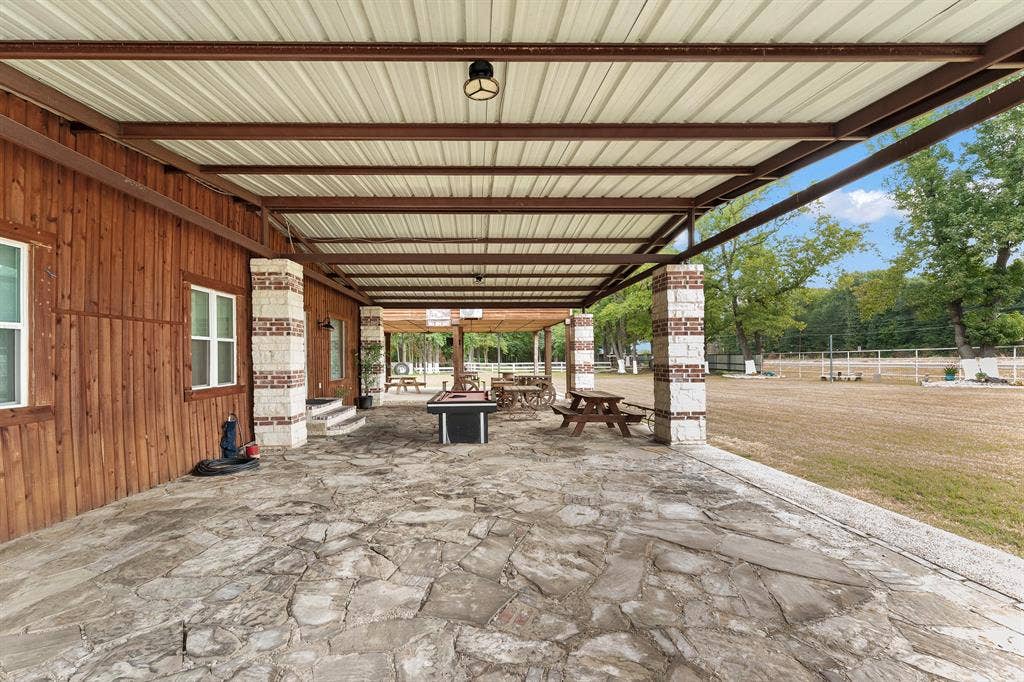 5989 State Highway 31 E, Murchison, TX 75778 Expansive covered patio featuring a flagstone surface, brick and stone columns, and a metal roof structure