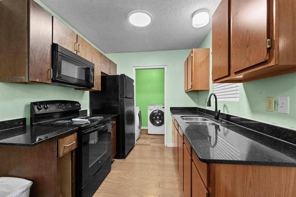 5989 State Highway 31 E, Murchison, TX 75778 Galley kitchen featuring wood cabinetry, black appliances, dark countertops, and wood-finish flooring