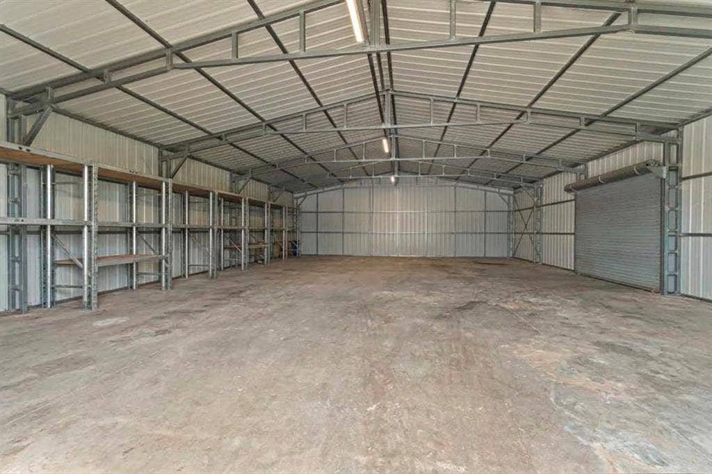5989 State Highway 31 E, Murchison, TX 75778 Expansive metal structure featuring a concrete floor, built-in shelving, corrugated metal walls, a roll-up door, and exposed metal trusses