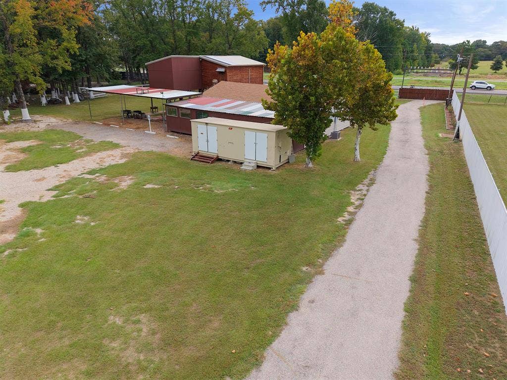 5989 State Highway 31 E, Murchison, TX 75778 Expansive grounds with a gravel driveway, mature trees, a perimeter fence, and multiple outbuildings