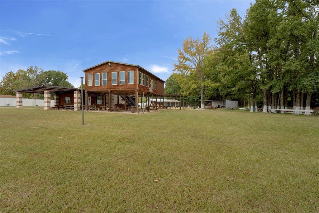 5989 State Highway 31 E, Murchison, TX 75778 Elevated wooden structure featuring multiple windows, a covered outdoor area with stone-clad columns, and a large grassy expanse