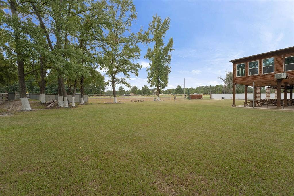 5989 State Highway 31 E, Murchison, TX 75778 Expansive grassy area with mature trees, a multi-story wood-sided structure, and a fenced perimeter
