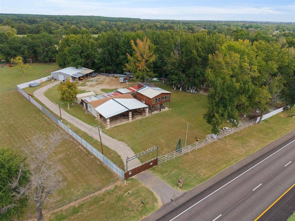 5989 State Highway 31 E, Murchison, TX 75778 Expansive property featuring a gravel driveway, multiple outbuildings, fenced perimeter, and a wooded backdrop