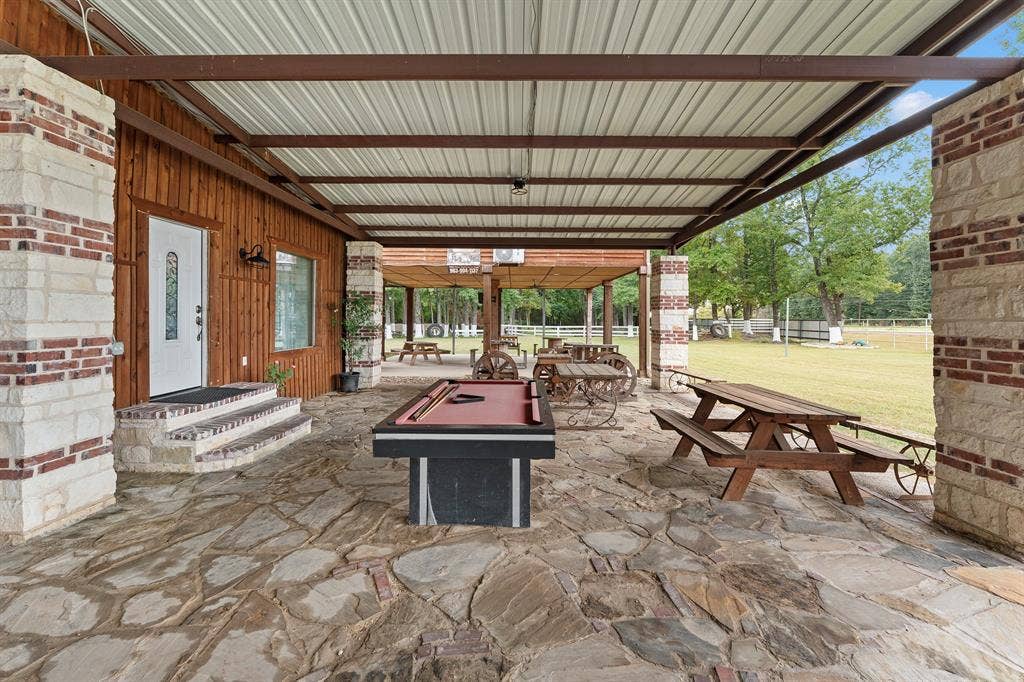 5989 State Highway 31 E, Murchison, TX 75778 Expansive covered patio featuring a metal roof, flagstone flooring, and stone columns with brick accents