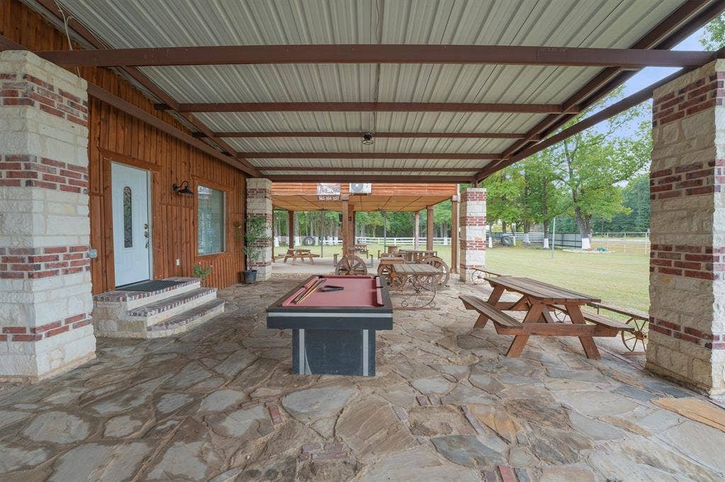 5989 State Highway 31 E, Murchison, TX 75778 Expansive covered patio featuring flagstone flooring, wood paneling, and stone columns with brick accents