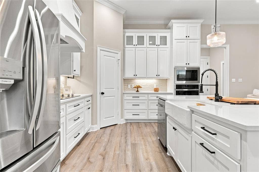 10201 Castleberry Lane, Waco, TX 76712 White cabinetry with black hardware, stainless steel appliances, wood-finish flooring, white countertops, and a farmhouse-style sink