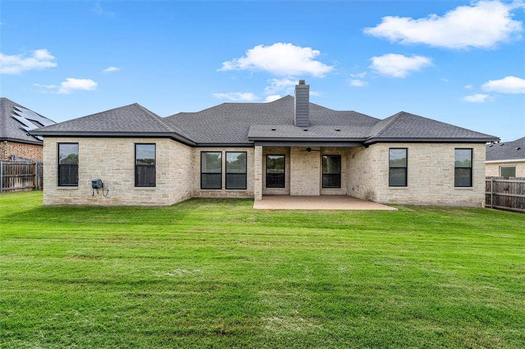 10201 Castleberry Lane, Waco, TX 76712 Extensive lawn space, stone exterior, black-framed windows, dark shingle roof, and a covered concrete patio