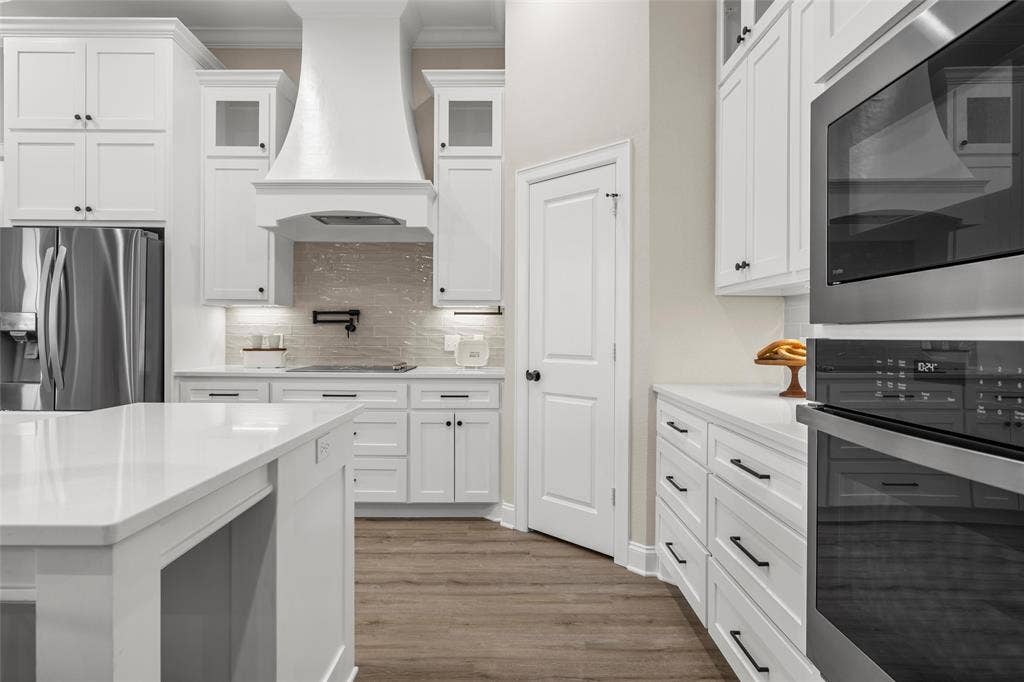 10201 Castleberry Lane, Waco, TX 76712 White shaker cabinetry, quartz countertops, stainless steel appliances, wood-finish flooring, and a decorative range hood