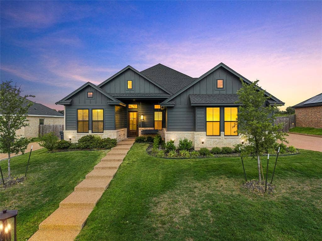 10201 Castleberry Lane, Waco, TX 76712 Contemporary exterior featuring dark gray vertical siding, stone veneer accents, multiple large windows, and a paved walkway