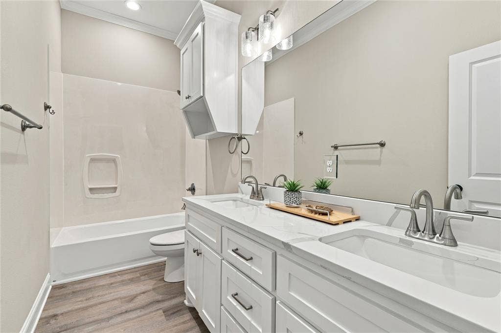 10201 Castleberry Lane, Waco, TX 76712 Dual vanity with integrated sinks and brushed nickel faucets, white cabinetry, a built-in bathtub with a wall surround, and wood-finish flooring