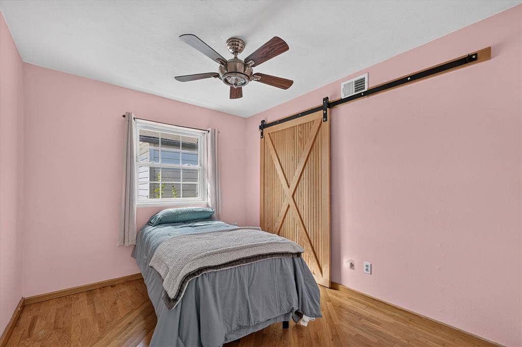 Wood-finish flooring, single window, wood barn door, and a ceiling fan with light