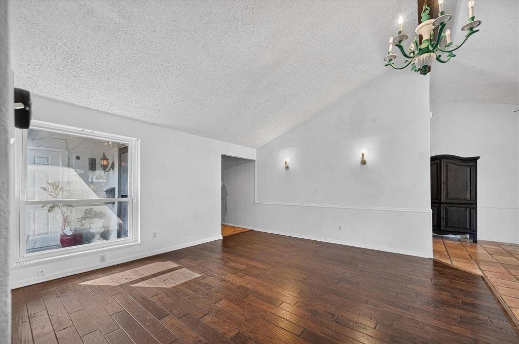 Vaulted ceiling, wood-finish flooring, white walls, picture window, and chandelier