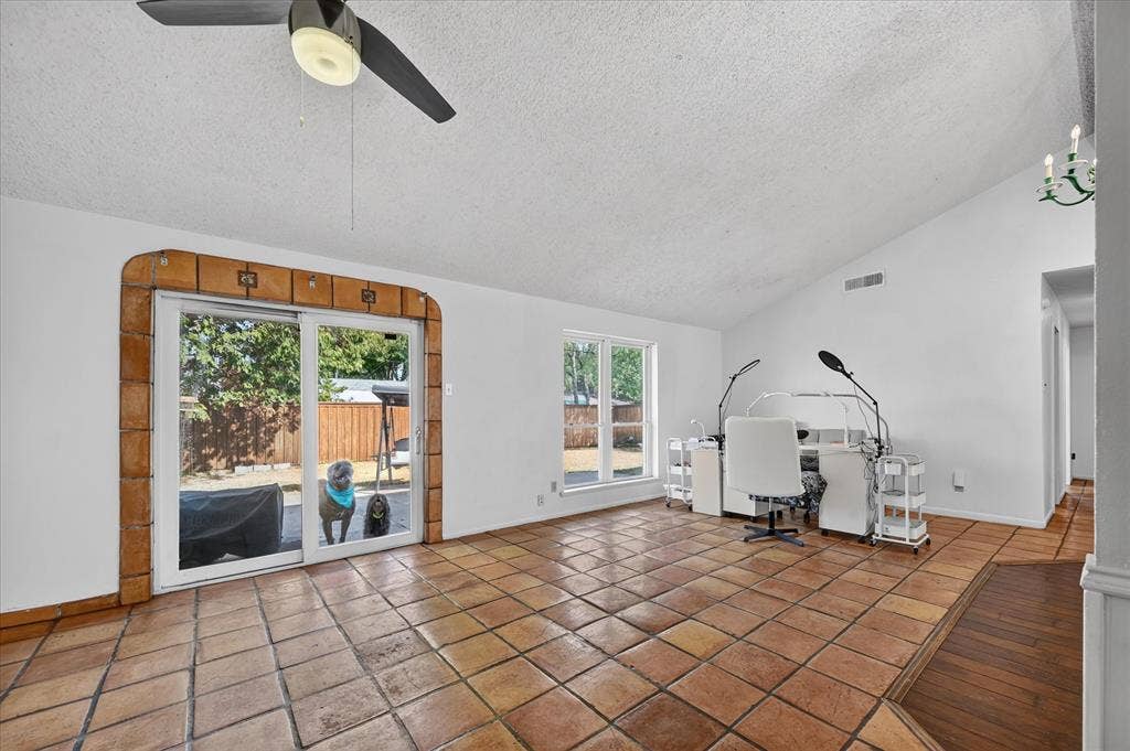 Vaulted ceiling with an attached ceiling fan, terra cotta tile flooring, white walls, and a sliding glass door
